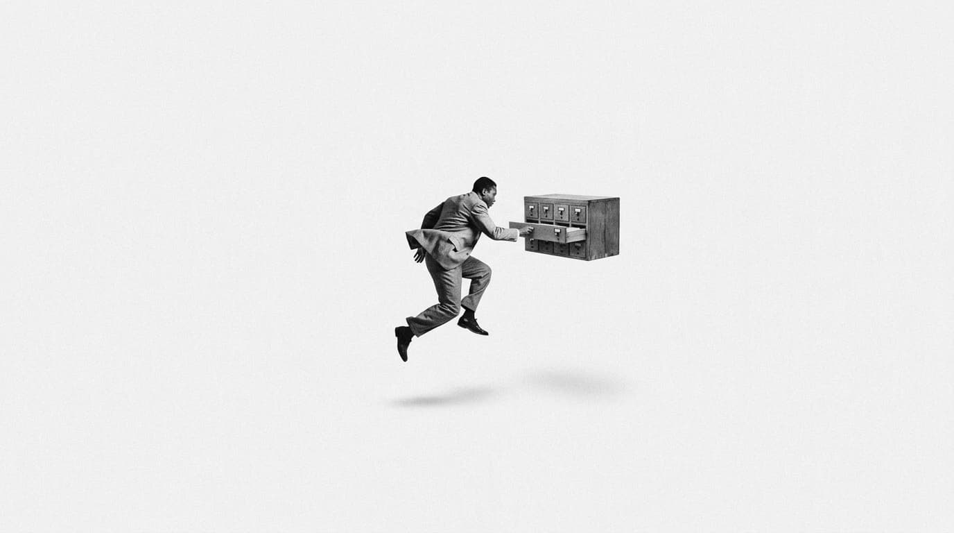 A man in a suit leaping to pull a drawer from a floating card catalogue