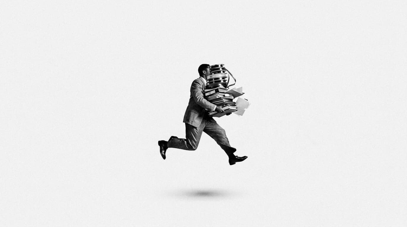 A man in a suit leaping while carrying a tall stack of film reels and folders